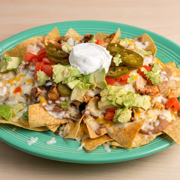 Chicken nachos with melted cheese, refried beans, avocado, tomatoes, jalapeños, and sour cream.