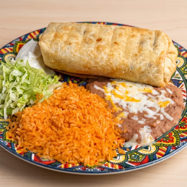 A colorful plate holds a large burrito, refried beans with cheese, orange rice, shredded lettuce, and sour cream.