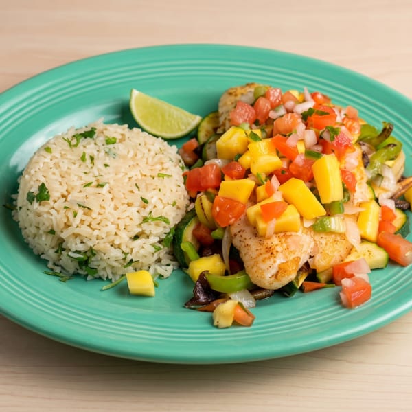 Grilled fish with mango salsa, rice, and vegetables on a teal plate.