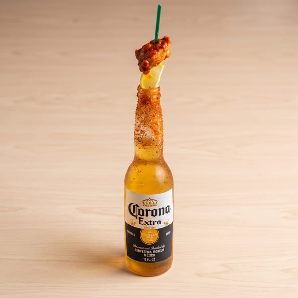 Corona Extra beer bottle with a chili-lime rim, lemon slice, and a chicken wing on a skewer.
