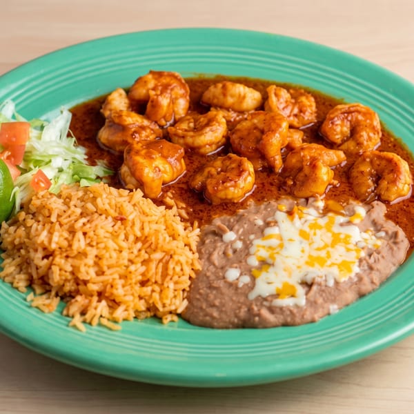 Shrimp in red sauce with rice, refried beans, and a side salad with lime on a green plate.